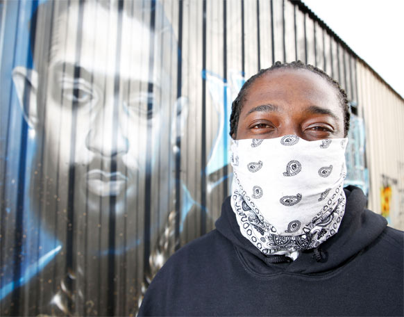 Man in bandana standing in front of graffitti.