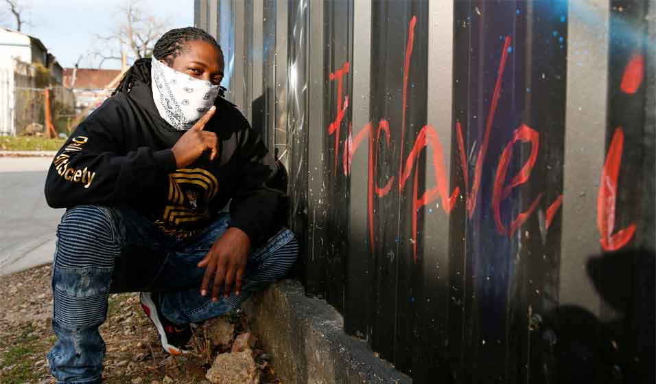 Man in bandana kneeling in front of graffitti.